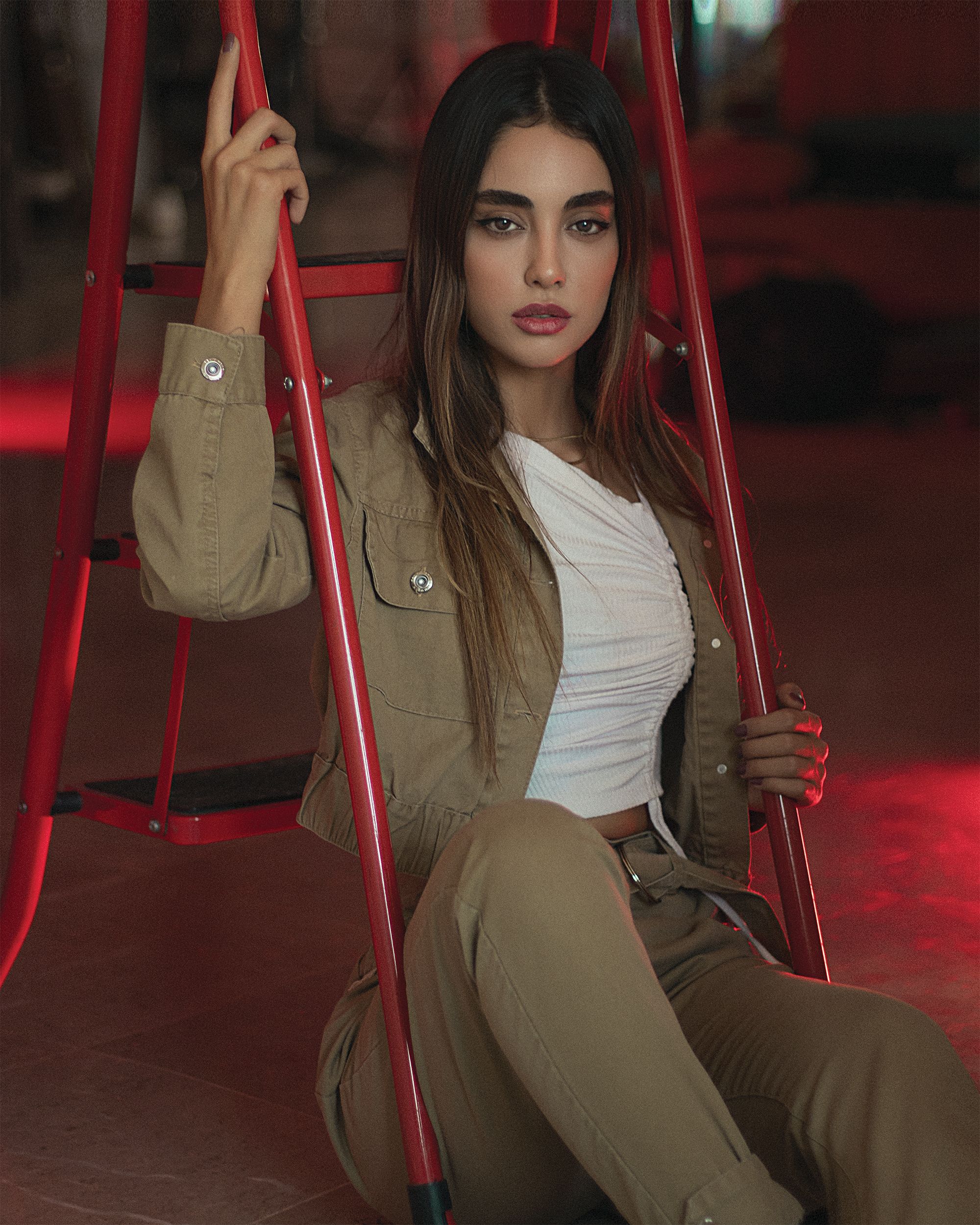 Elegant woman posing on a red stepladder indoors with a moody atmosphere.