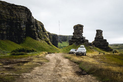 Vehicles on Green Grass Field Near Rock Formations