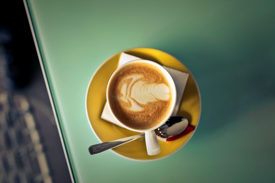 Top view of a latte with intricate art on a yellow saucer at a café.