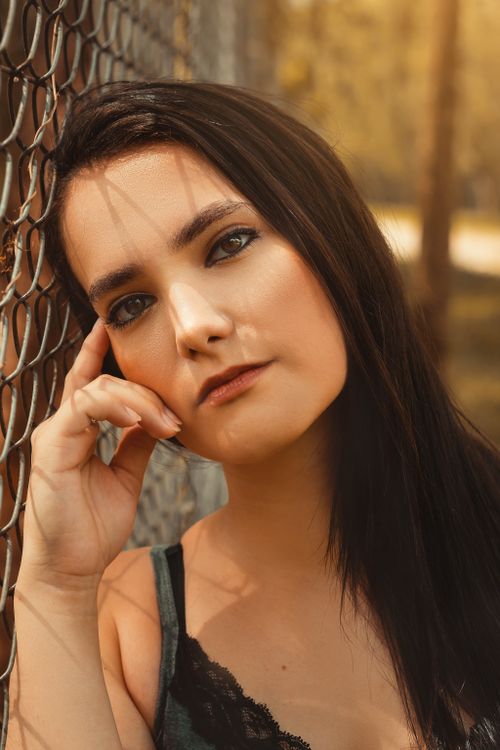 Free Outdoor portrait of a thoughtful woman leaning on a fence, captured in warm tones. Stock Photo