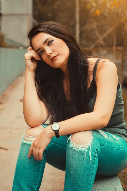 Free Casual portrait of a woman in a green top and ripped jeans, sitting outdoors with a thoughtful expression. Stock Photo