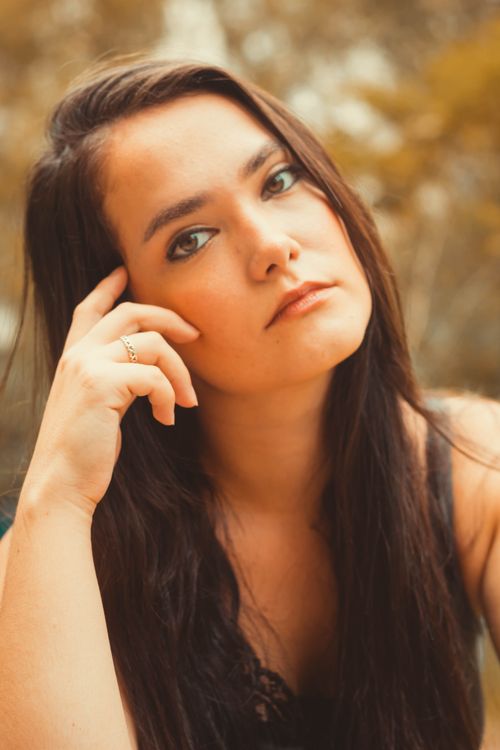 Free Elegant portrait of a woman posing outdoors with a thoughtful expression and warm tones. Stock Photo