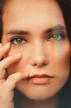 A captivating close-up portrait of a woman with a rainbow reflection across her face, highlighting her eyes and makeup.