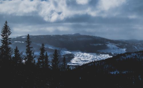 Free A serene winter landscape featuring snow-capped mountains and a pine forest under a cloudy sky. Stock Photo