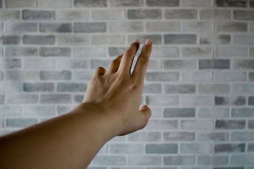 회색 콘크리트 벽돌 근처 사람의 왼손