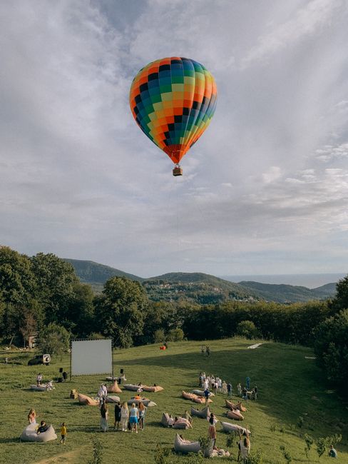 Colorful hot air balloon floating above a green field with people enjoying a scenic outdoor event.