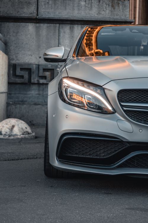 Free Close-up of a silver luxury car front with glowing headlights in an urban setting. Stock Photo
