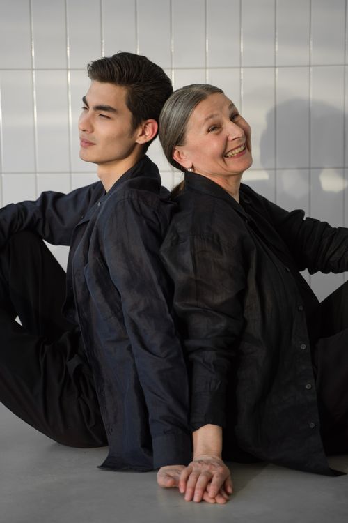 Free A joyful mother and son sitting back to back indoors, wearing black clothes and sharing a tender moment. Stock Photo