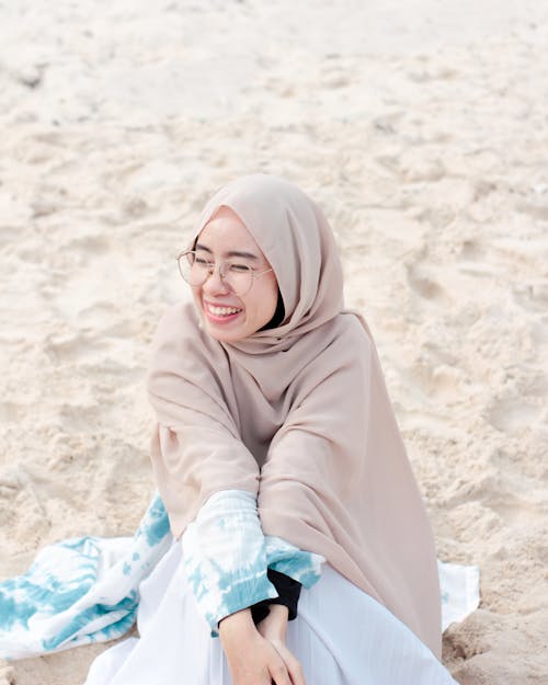 A Woman Wearing Hijab Sitting on the Sandy Shore of a Beach