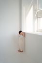 Woman in White Long Sleeve Shirt Standing Beside Window