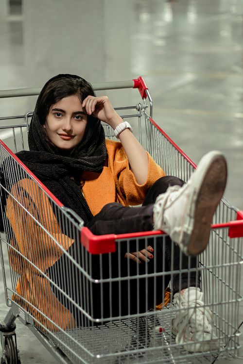 Free A young woman with a headscarf sits playfully in a shopping cart indoors. Stock Photo