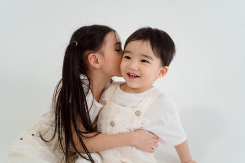 Free Cute siblings sharing a moment of joy while whispering with a clean white background, showcasing their bond. Stock Photo