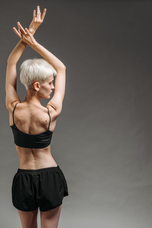 Free A stylish woman poses with raised arms in a sleek studio setting, capturing simplicity and elegance. Stock Photo