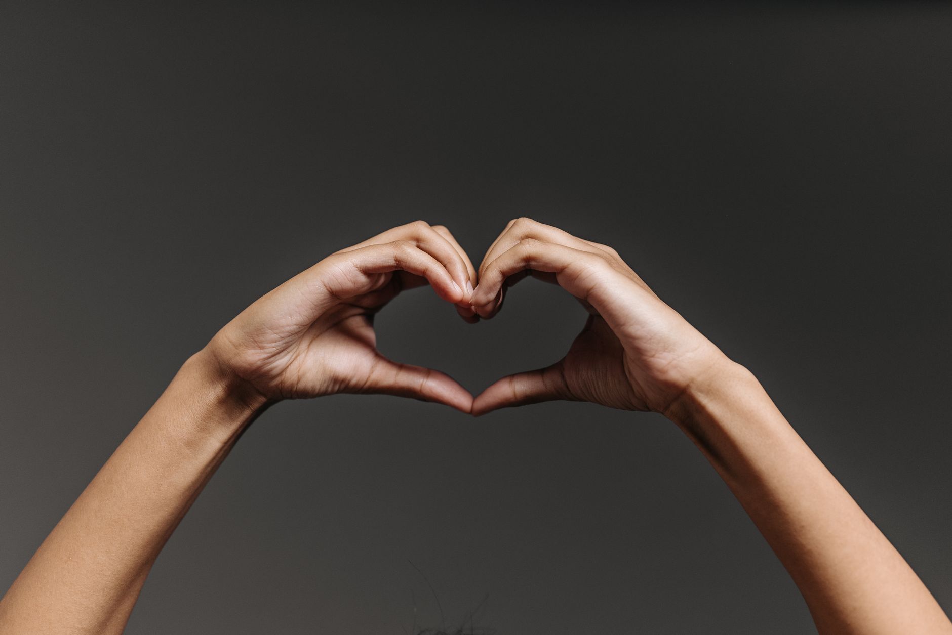 Close-up of hands forming a heart shape gesture against a gray background in a studio setting.