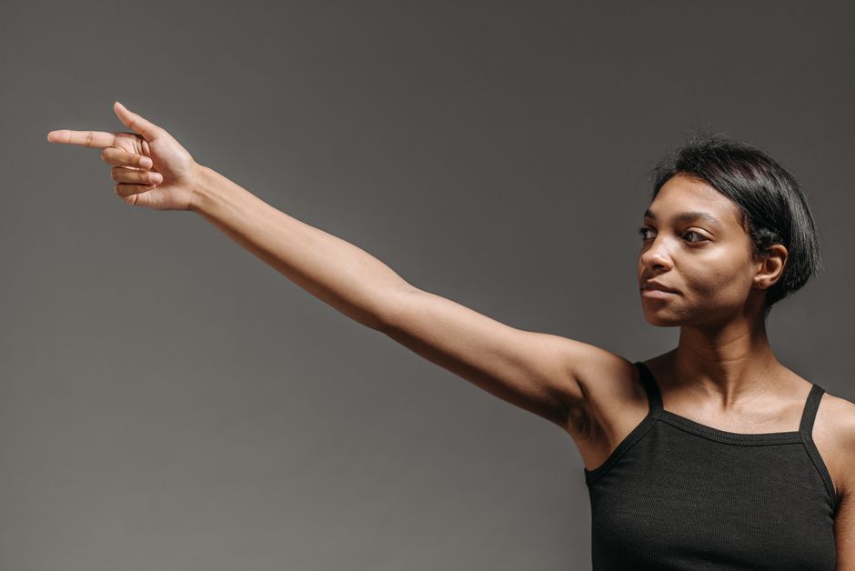 A woman confidently pointing against a gray background in a studio setting.