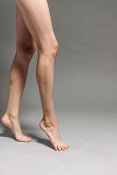 Close-up of bare legs on tiptoe against a simple backdrop, highlighting skin tone and texture.