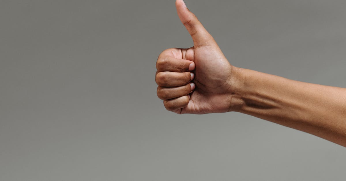 A close-up image of a hand making a thumbs up gesture against a neutral background.