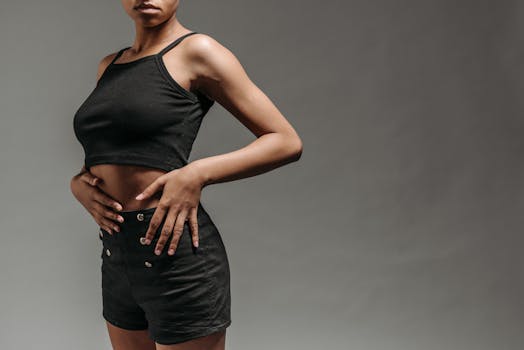 Studio portrait of a woman in black cropped top and shorts with hands on waist.