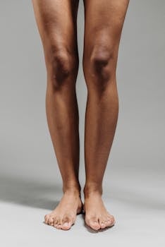 Close-up image of a person's bare legs and feet standing on a neutral background.