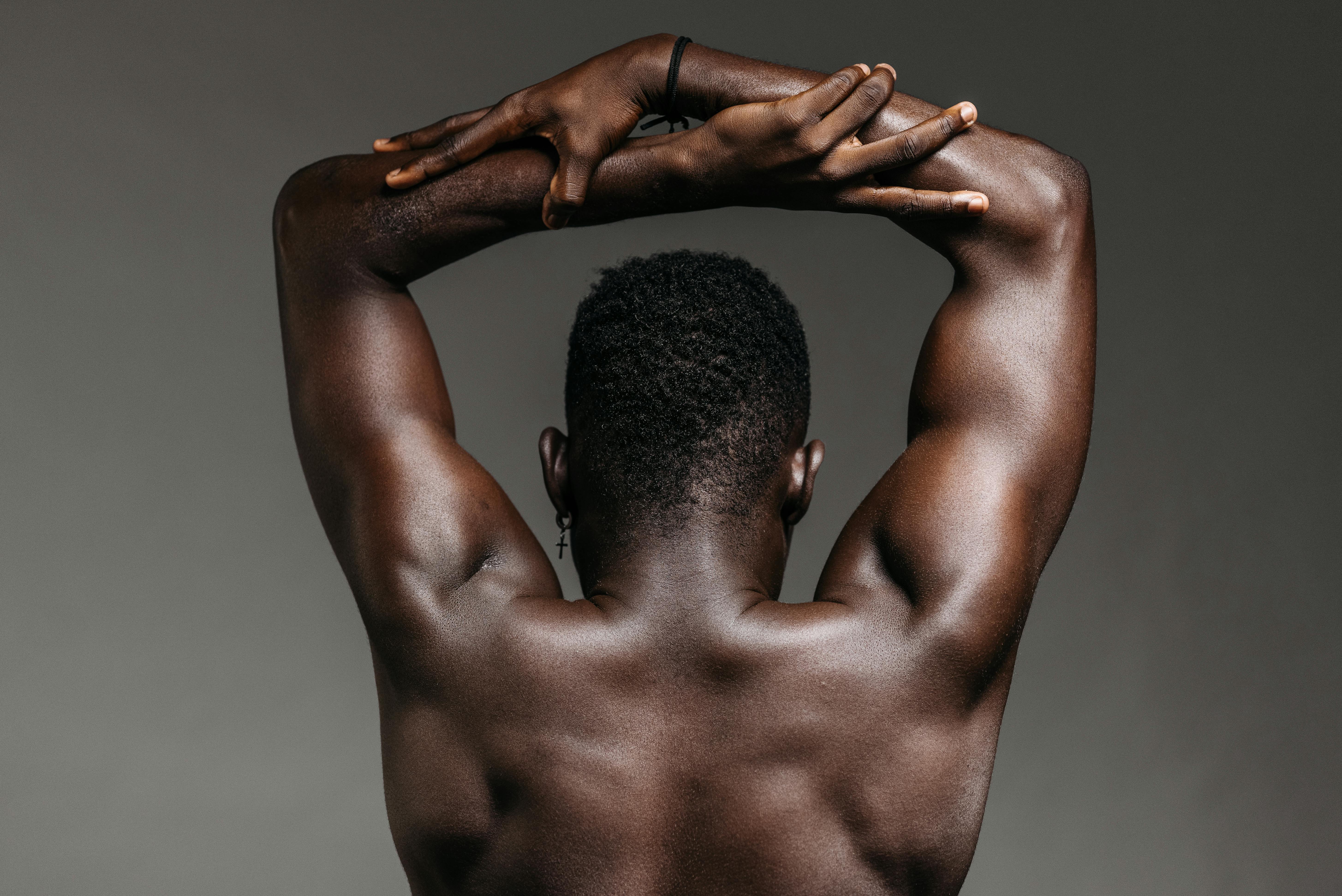 Close-up view of a shirtless African American man's muscular back with arms raised.