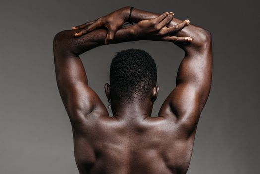 Close-up view of a shirtless African American man's muscular back with arms raised.