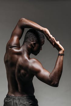 Brawny shirtless man with raised arms stretching against a dark gray background.