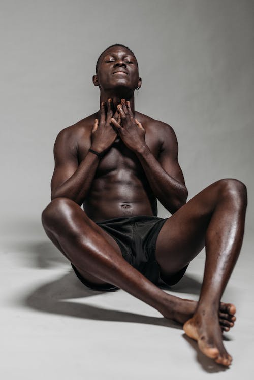 A Topless Man Wearing Black Short while Sitting on a White Surface 