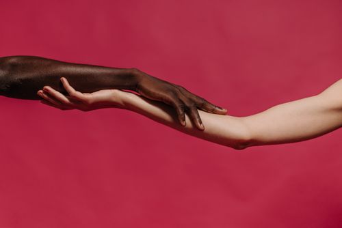 Free Embrace of two diverse hands against a vibrant red backdrop symbolizing unity. Stock Photo
