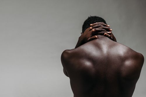 Free Back view of a brawny shirtless man with hands clasped on neck against a gray background. Stock Photo