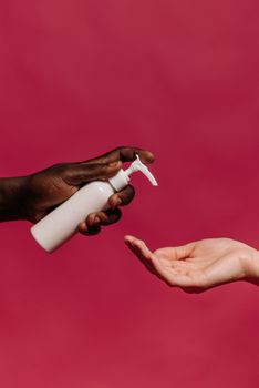 A close-up shot of two hands using a lotion dispenser against a red background, emphasizing hygiene.