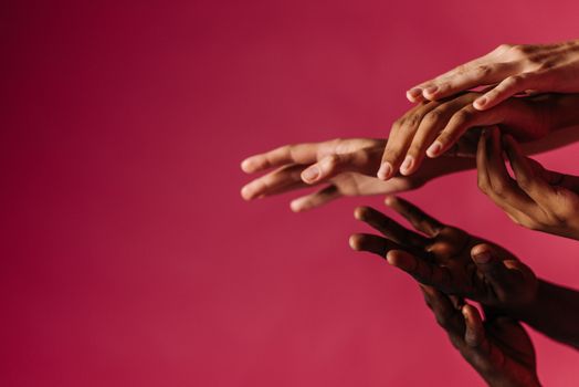 Close-up of multiple diverse hands reaching out in a studio setting on a pink background.