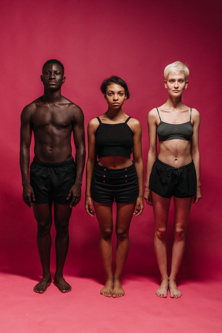 A diverse group of three individuals posing against a red studio backdrop, showcasing different ethnicities and body types.
