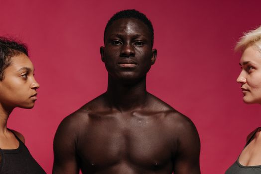Three diverse models posing seriouly against a bright pink background in a studio.