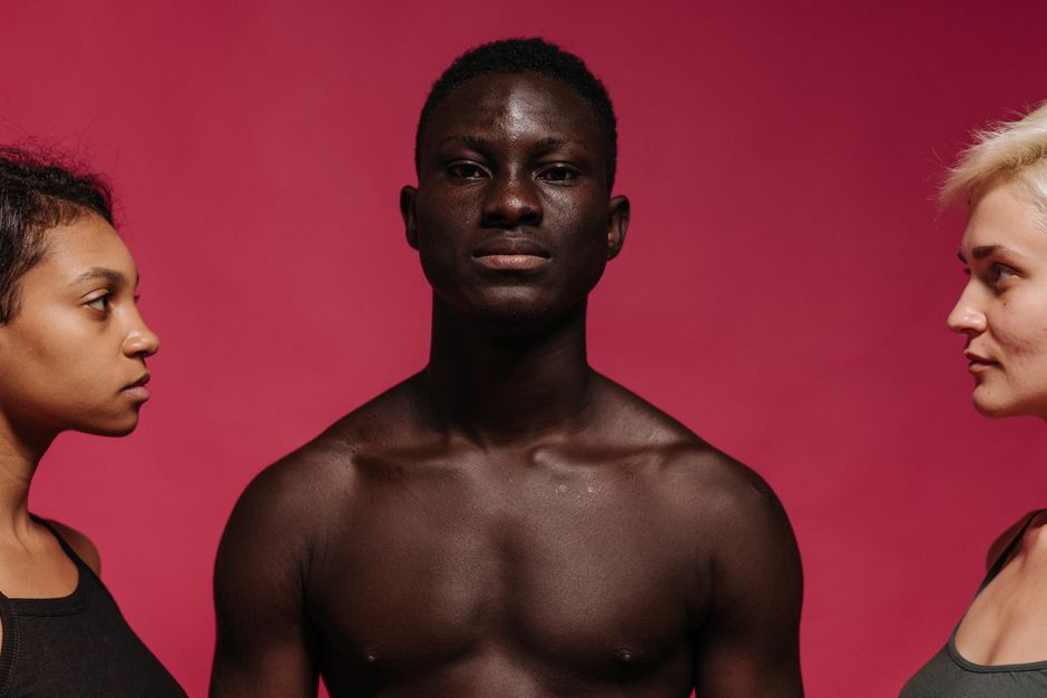 Three diverse models posing seriouly against a bright pink background in a studio.