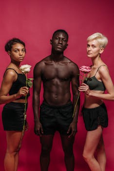 Three diverse individuals posing with roses against a red backdrop in a studio setting.
