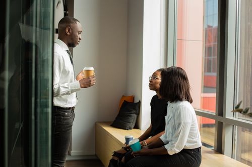 Free Three professionals discussing ideas in a bright office space with coffee. Stock Photo