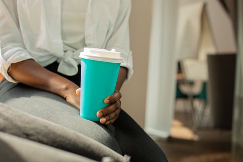 Free Close-up of a person holding a blue disposable coffee cup in a cozy indoor setting. Stock Photo