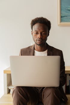 Man in a business suit working on a laptop at a desk indoors, showing focus and dedication.
