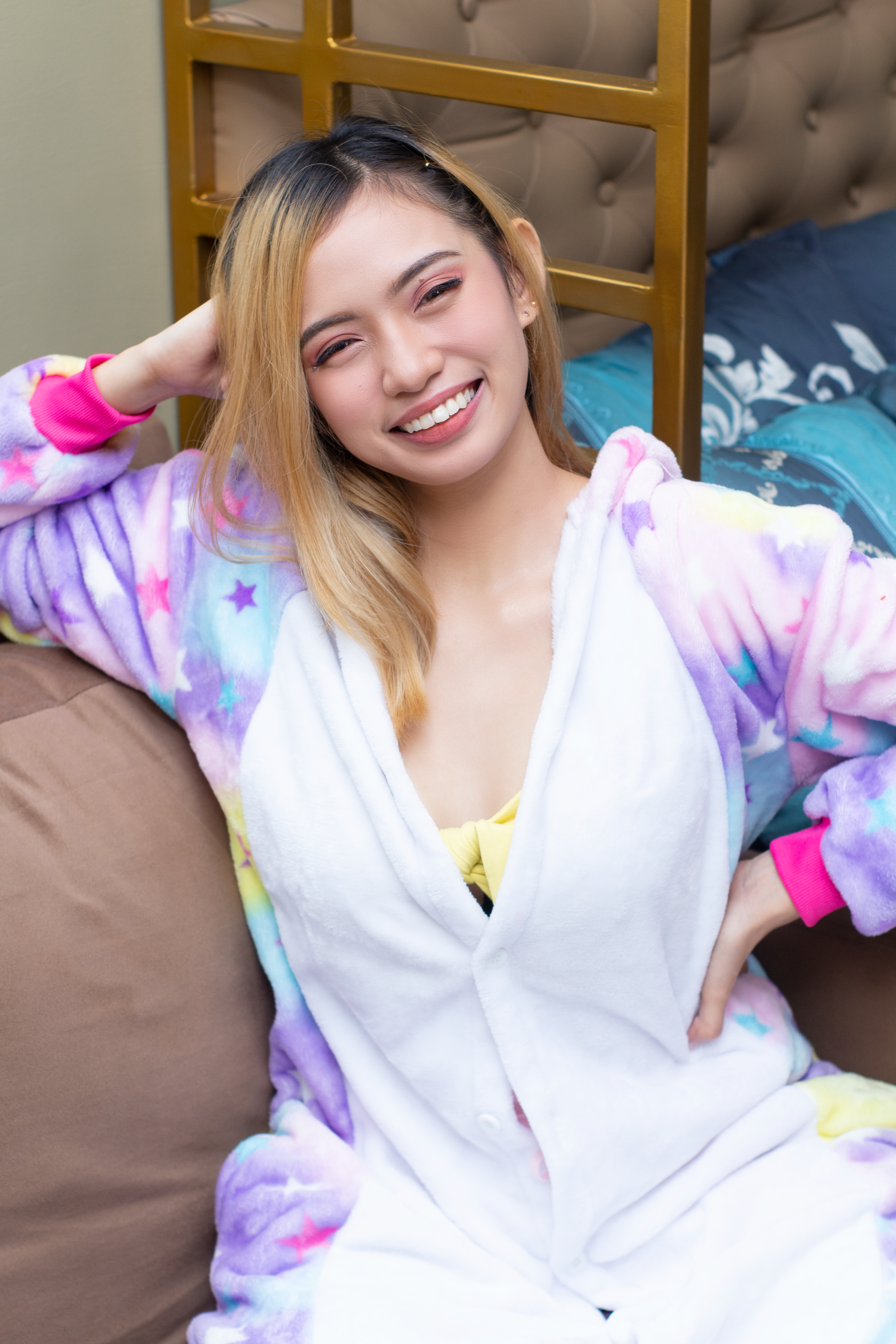 A cheerful woman poses in a colorful robe, sitting comfortably indoors and smiling brightly.
