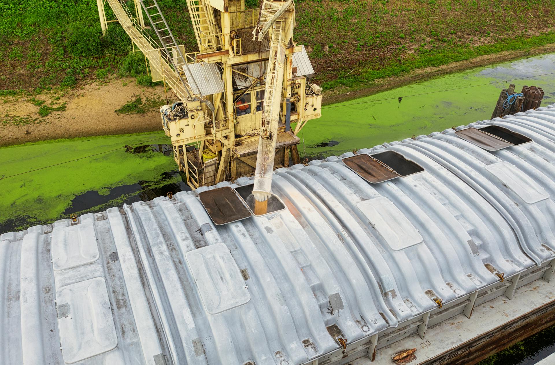 Drone shot showing a grain barge being loaded at a dock. Ideal for industrial and agricultural themes.