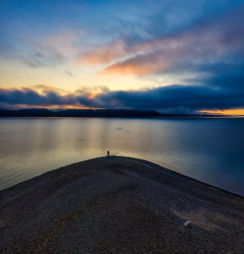 Person Standing Near the Calm Body of Water During Sunset 