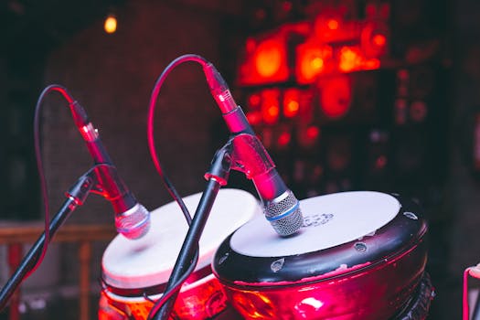 A close-up view of bongo drums with microphones on stage, illuminated by dynamic red lighting.