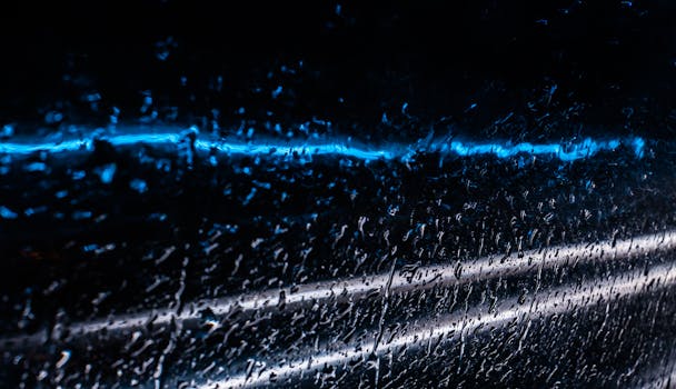 Captivating close-up of raindrops on a window reflecting neon blue light at night.