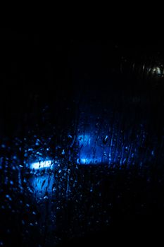 Abstract image of rain-soaked glass highlighting blue light through droplets.