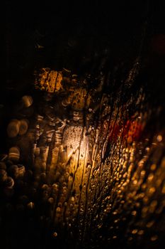Abstract view of water droplets on glass with warm lighting and bokeh effect, creating a moody atmosphere.