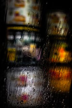 Blurry city lights seen through rain-soaked window, capturing a moody night atmosphere.