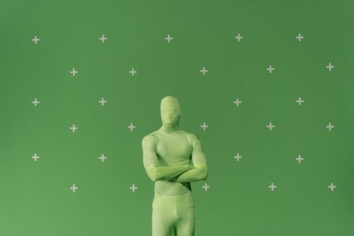 Free Person in a green chroma key suit standing against a marked green screen in a studio. Stock Photo