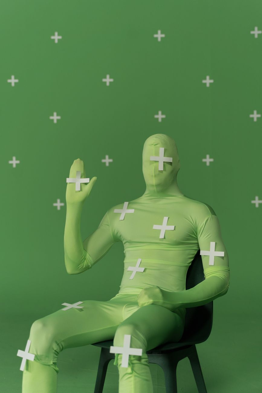 Persoon in chroma key bodysuit zit op een stoel in een studio-opstelling voor visuele effecten en post-productie.