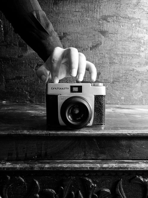 Free Black and white photo of a hand holding a vintage camera on a wooden surface. Stock Photo