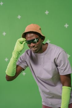 A stylish man in a bucket hat and gloves poses in a green screen studio with sunglasses. — photo by cottonbro studio